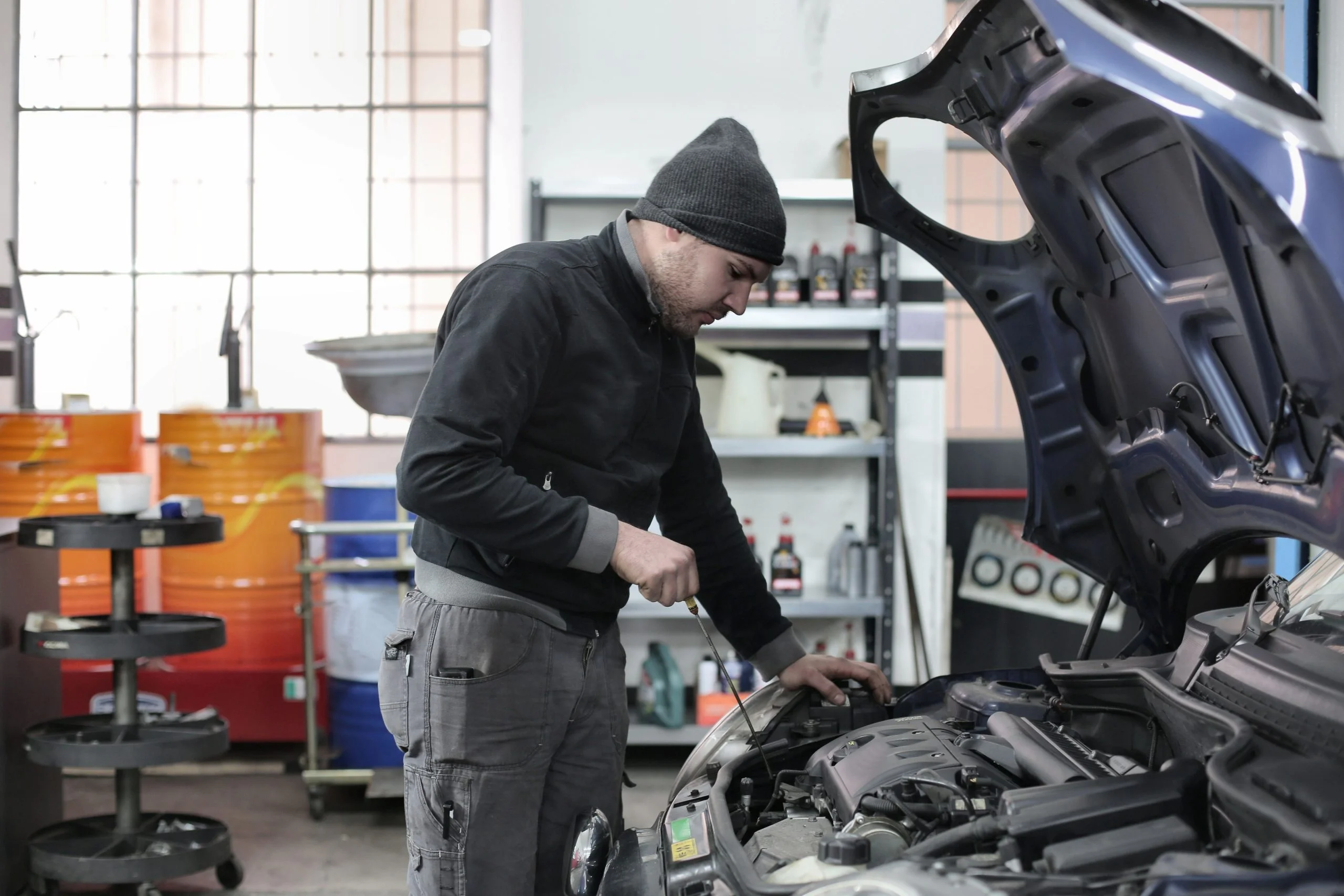 Auto mechanic inspecting a vehicle engine under an open hood in a professional automotive repair shop.
