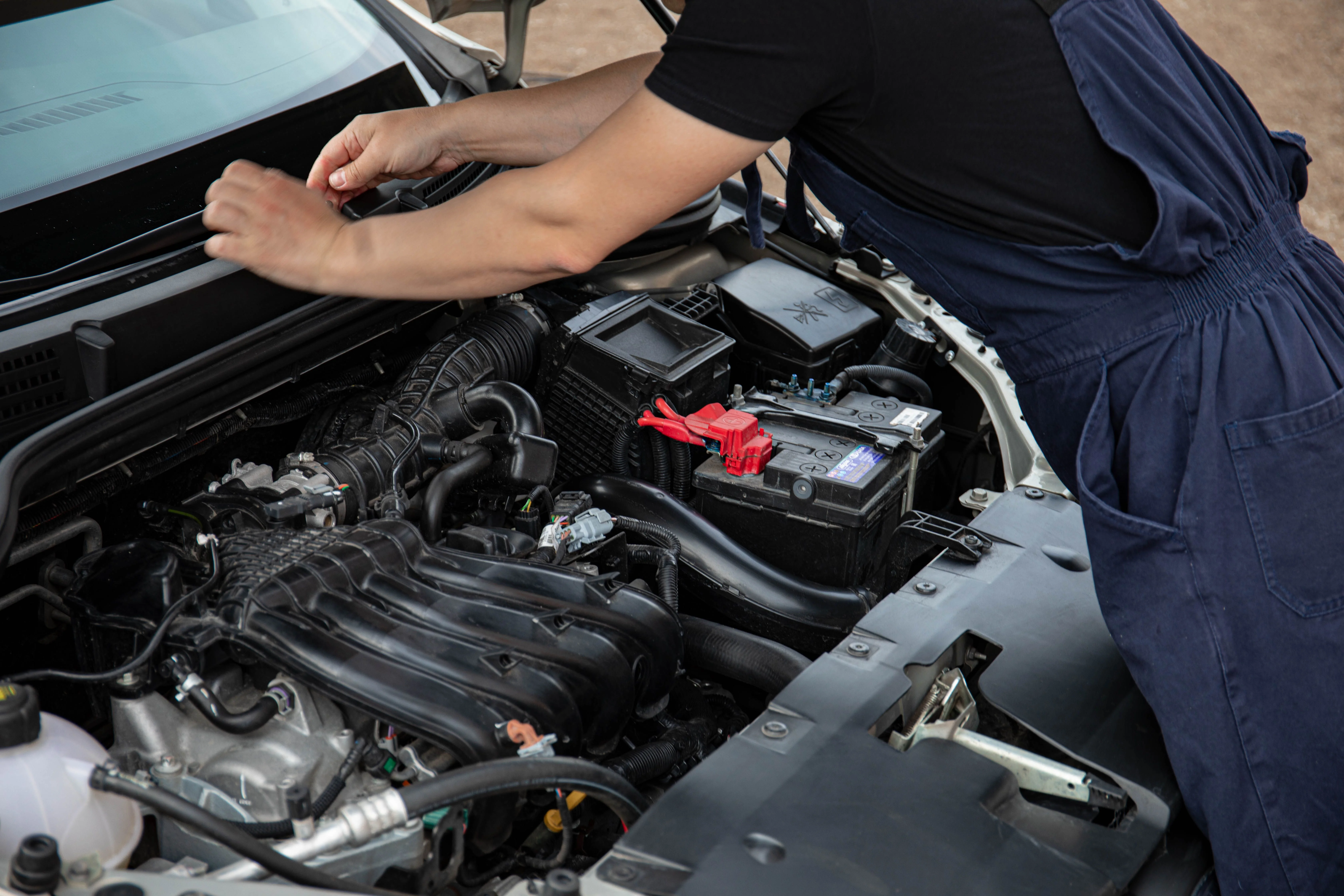 Automotive technician inspecting a car battery and engine components during vehicle maintenance.