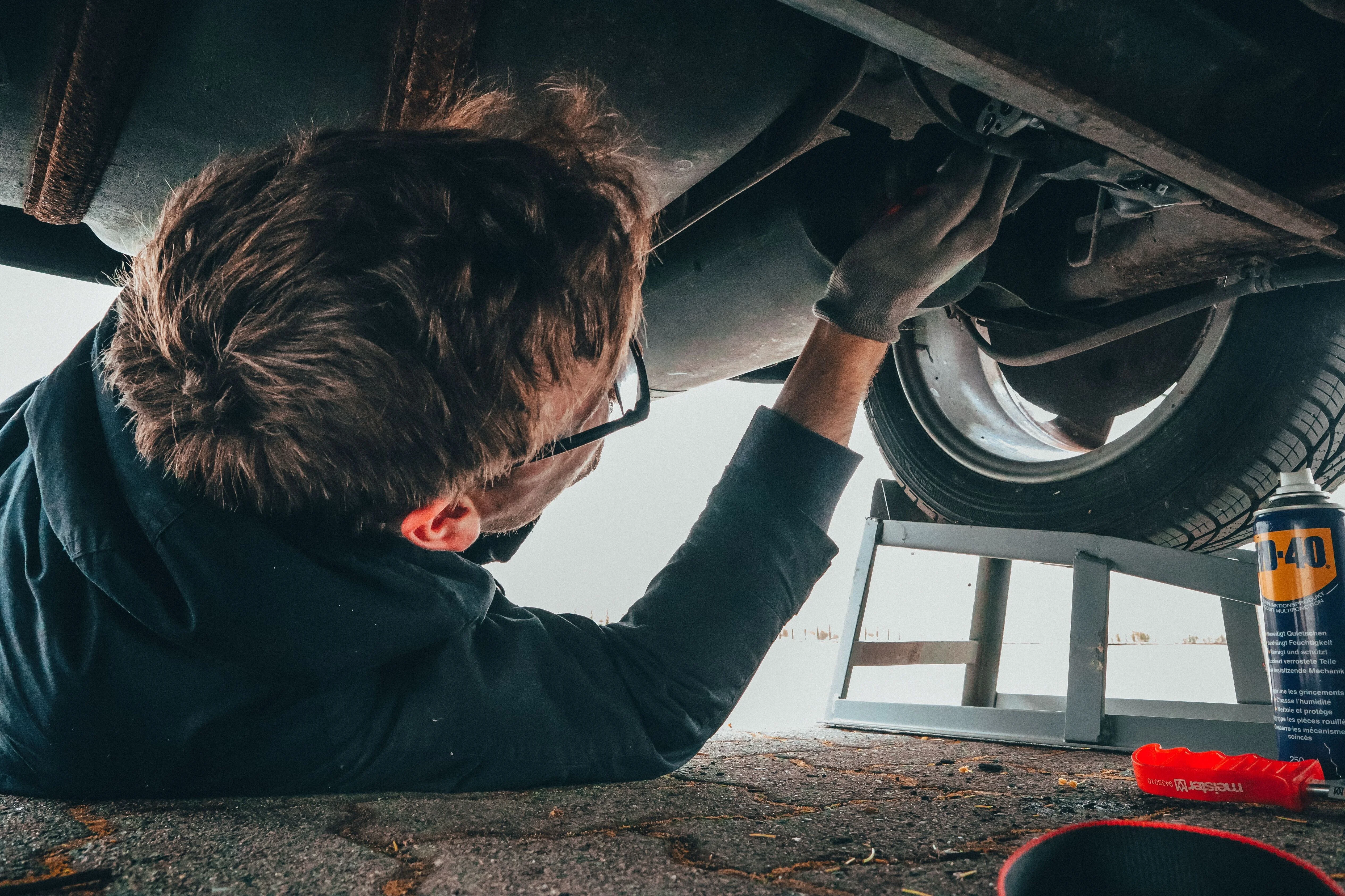 Automotive technician inspecting and repairing vehicle undercarriage components during maintenance service.
